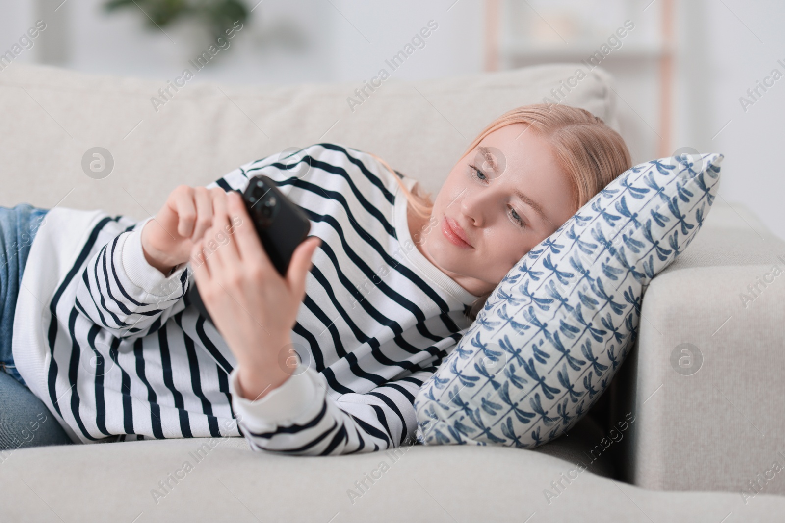 Photo of Beautiful woman using smartphone on sofa indoors