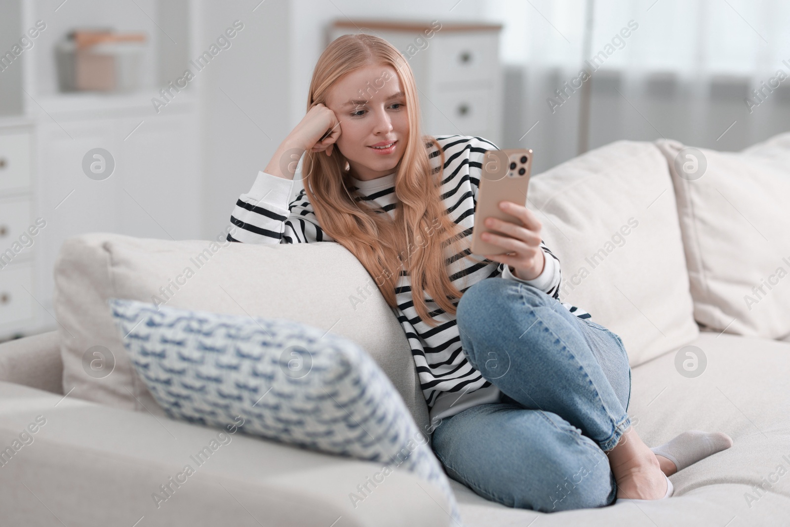 Photo of Smiling woman using smartphone on sofa indoors