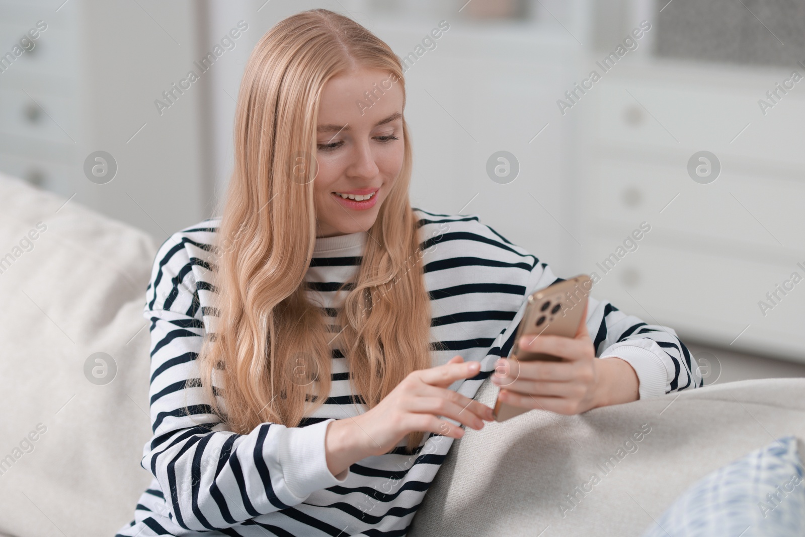 Photo of Smiling woman using smartphone on sofa indoors