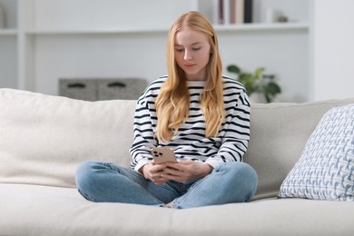 Beautiful woman using smartphone on sofa indoors