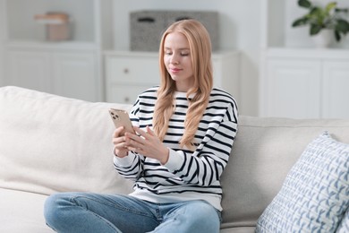 Beautiful woman using smartphone on sofa indoors