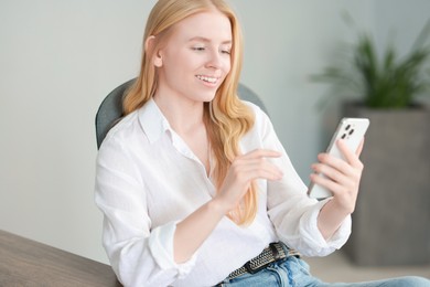 Smiling woman using smartphone at table in office