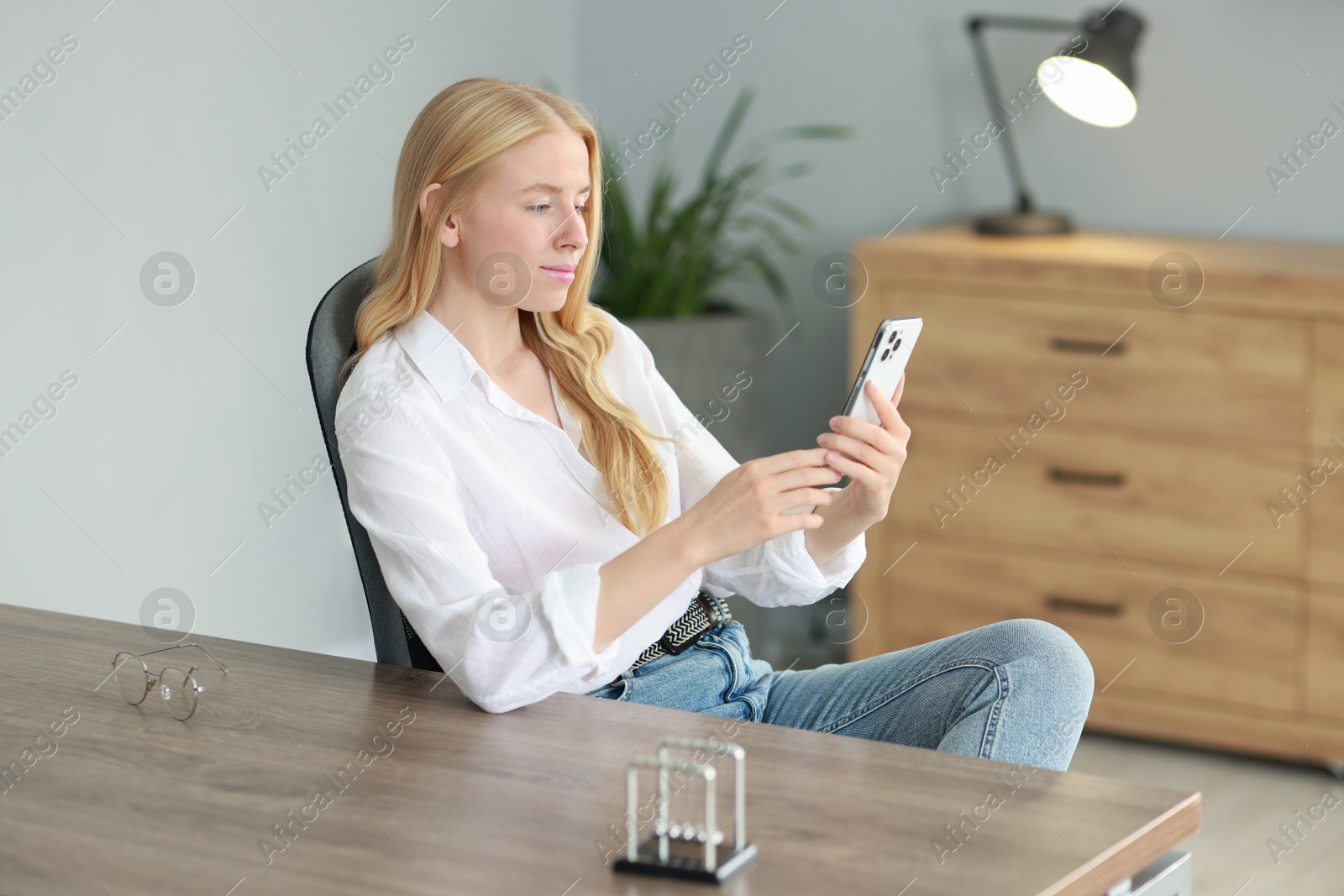 Photo of Beautiful woman using smartphone at table in office