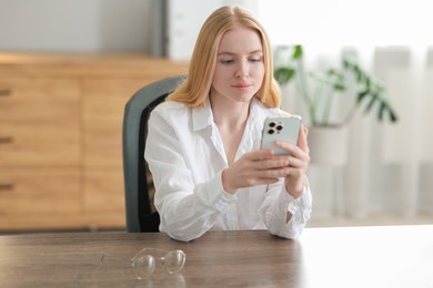 Photo of Beautiful woman using smartphone at table in office