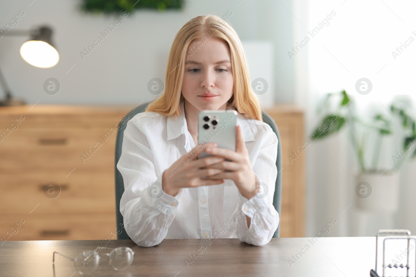 Photo of Beautiful woman using smartphone at table in office