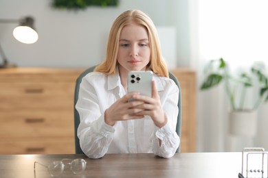 Beautiful woman using smartphone at table in office