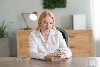 Photo of Beautiful woman using smartphone at table in office