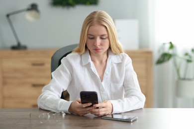 Beautiful woman using smartphone at table in office