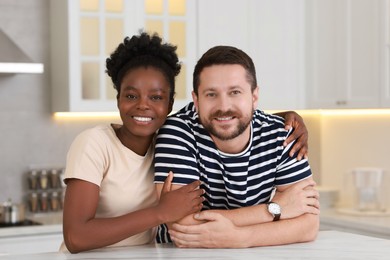 International relationships. Portrait of lovely couple at white marble table in kitchen