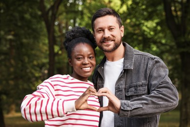 International relationships. Lovely couple making heart with hands outdoors