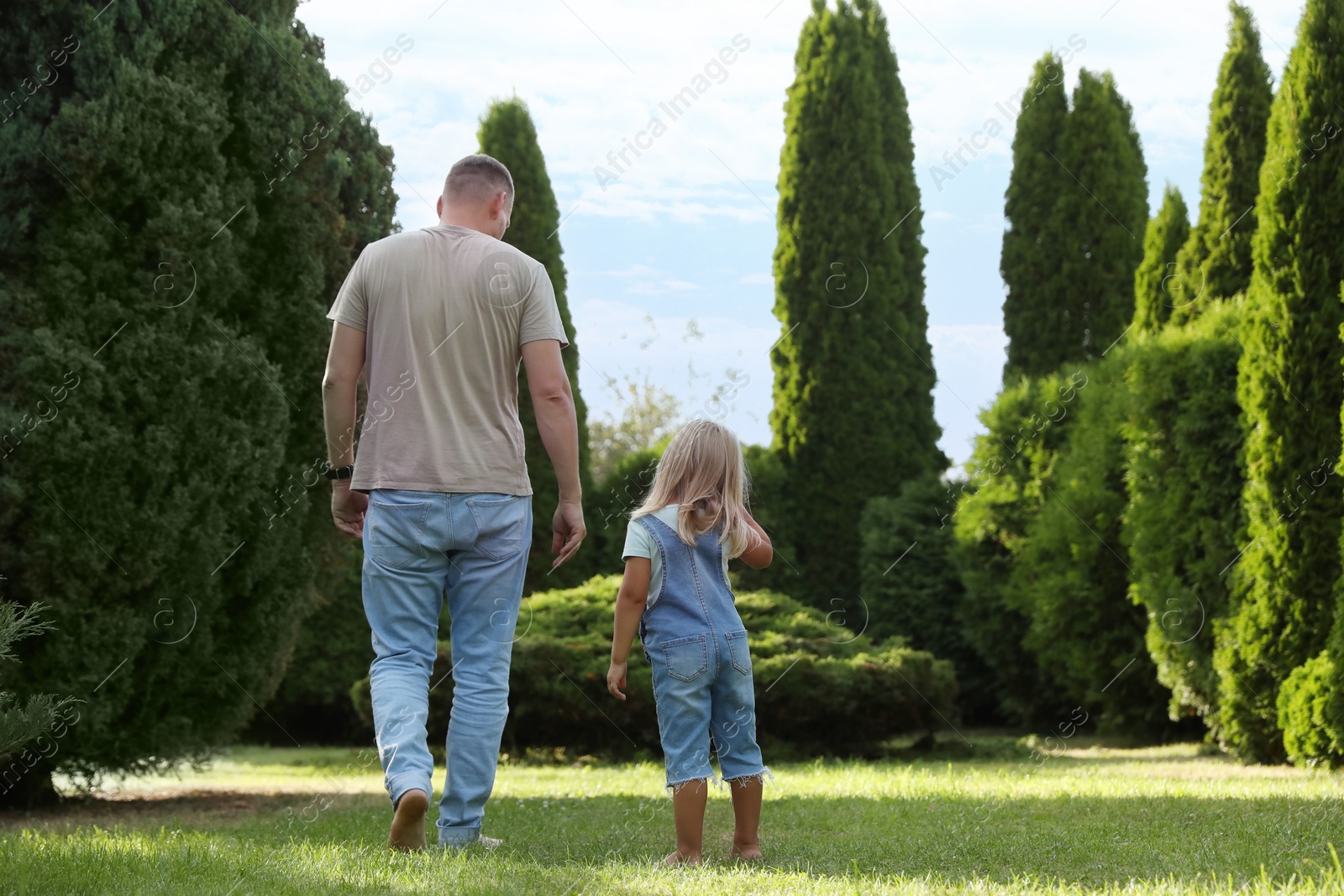 Photo of Father and his daughter spending time together on green lawn in park, back view