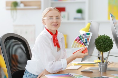 Photo of Designer with color samples working at table in office