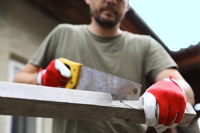 Man sawing wooden plank in backyard, closeup