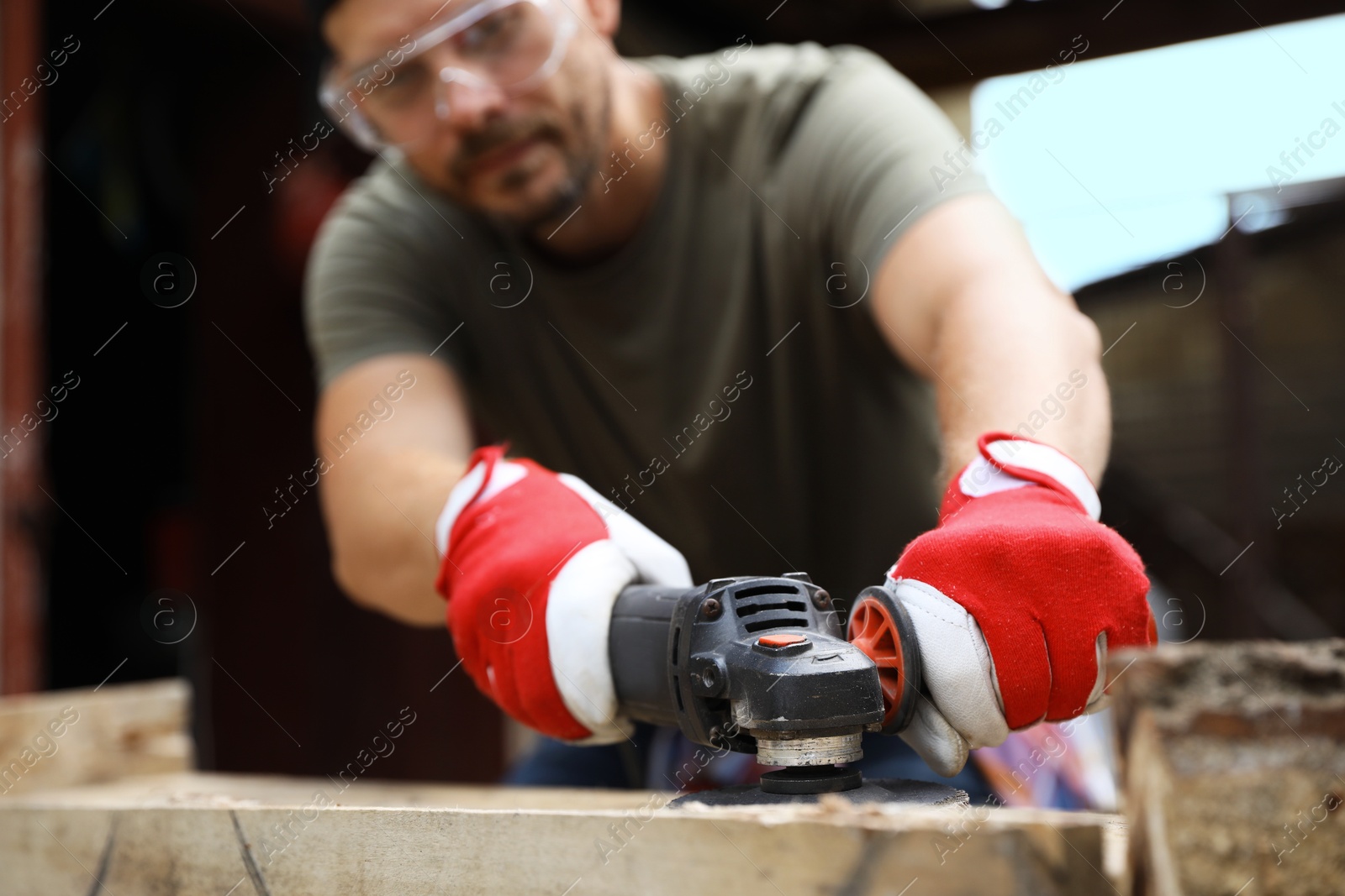 Photo of Man polishing wooden planks with angle grinder outdoors, selective focus