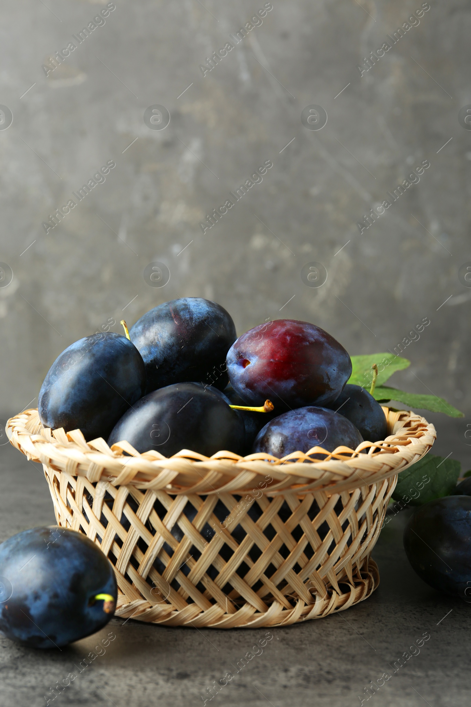 Photo of Tasty ripe plums in wicker bowl on grey textured table