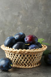 Photo of Tasty ripe plums in wicker bowl on grey textured table