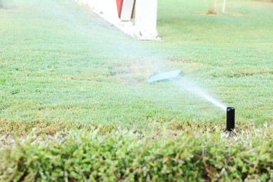 Photo of Automatic sprinkler watering green grass in garden