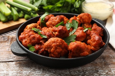 Photo of Baked cauliflower buffalo wings with parsley in baking dish on wooden table, closeup