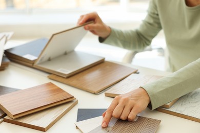 Photo of Woman choosing wooden flooring among different samples at table, closeup