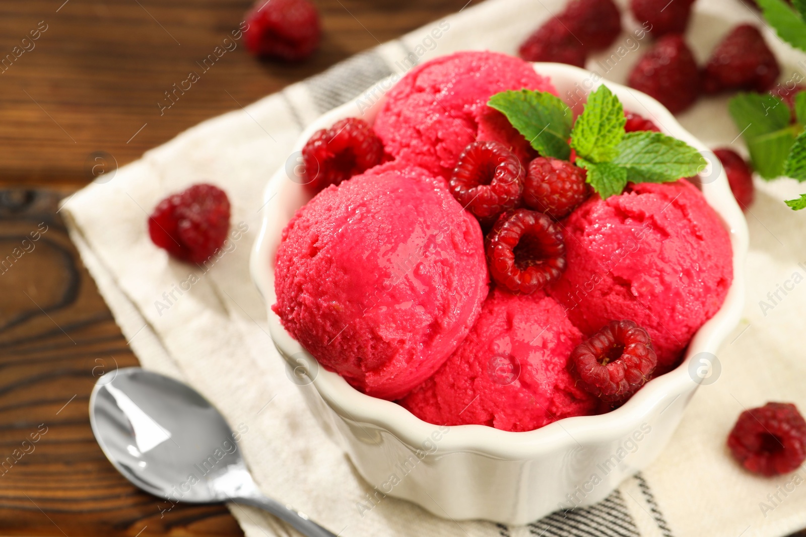 Photo of Delicious raspberry sorbet with fresh berries in bowl and spoon on wooden table, closeup