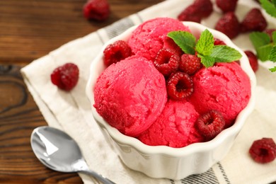 Photo of Delicious raspberry sorbet with fresh berries in bowl and spoon on wooden table, closeup