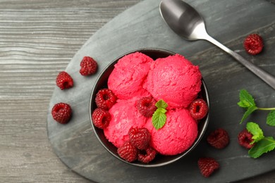 Photo of Delicious raspberry sorbet in bowl, fresh berries, mint and spoon on wooden table, top view