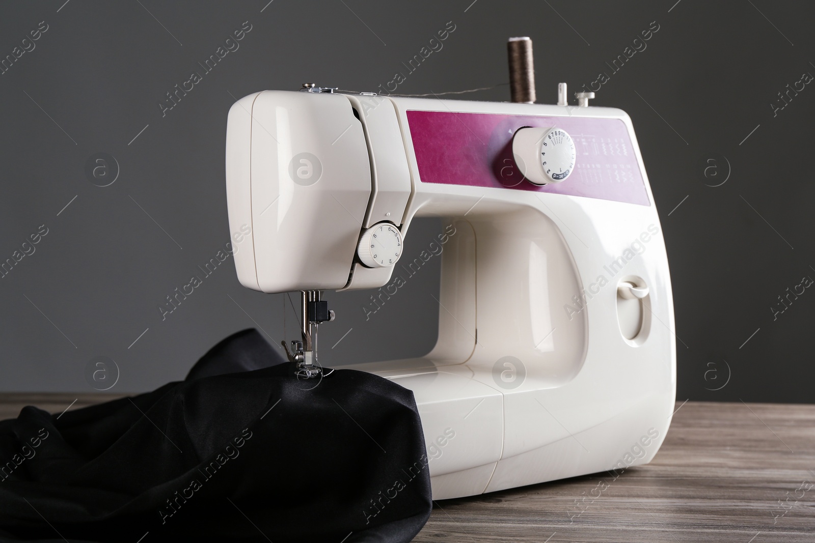 Photo of Sewing machine with black fabric on wooden table against gray background