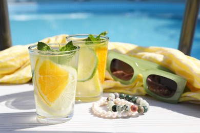 Photo of Tasty cocktail in glasses and sunglasses near swimming pool outdoors