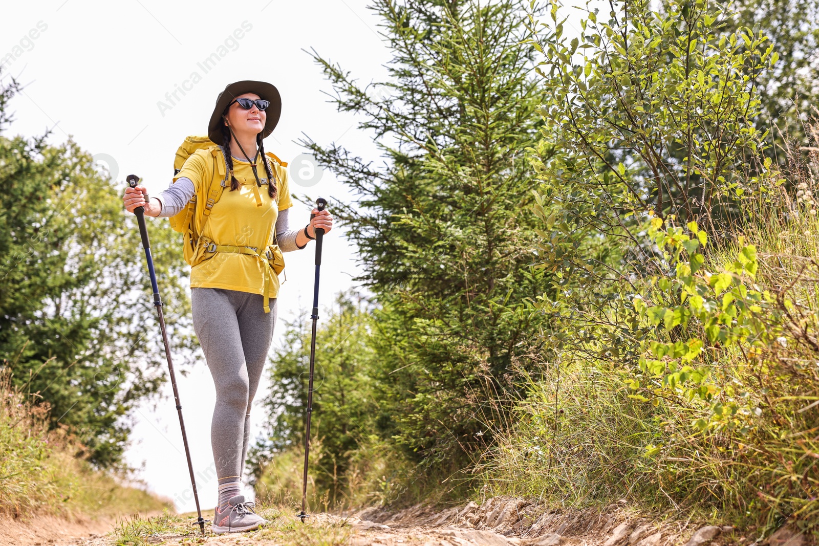 Photo of Young hiker with hat, sunglasses, trekking poles and backpack in mountains outdoors, space for text