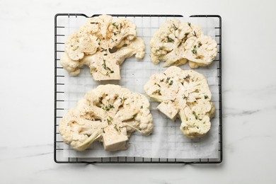 Photo of Uncooked cauliflower steaks and dill on white marble table, top view