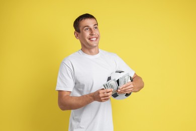 Photo of Happy man with money and soccer ball on yellow background