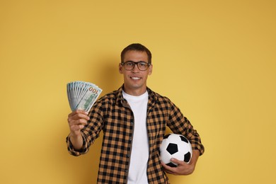 Photo of Happy man with money and soccer ball on yellow background