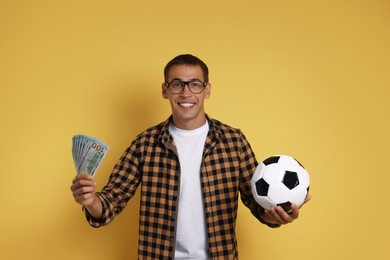 Happy man with money and soccer ball on yellow background