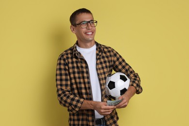 Happy man with money and soccer ball on yellow background