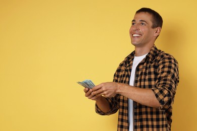 Happy man with money on yellow background, space for text