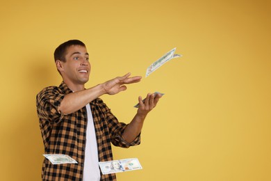 Happy man throwing money on yellow background, space for text