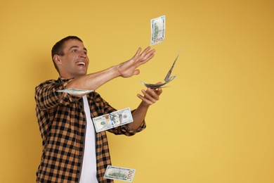 Happy man throwing money on yellow background, space for text