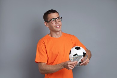 Happy man with money and soccer ball on grey background