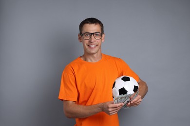 Happy man with money and soccer ball on grey background