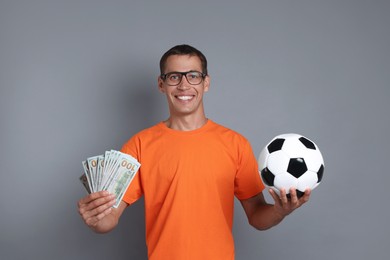 Happy man with money and soccer ball on grey background