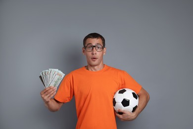 Man with money and soccer ball on grey background