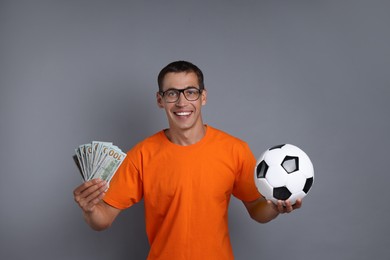 Happy man with money and soccer ball on grey background