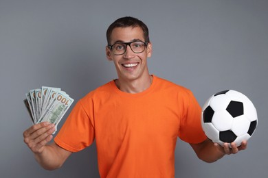 Happy man with money and soccer ball on grey background