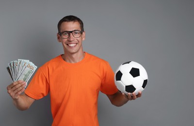 Happy man with money and soccer ball on grey background