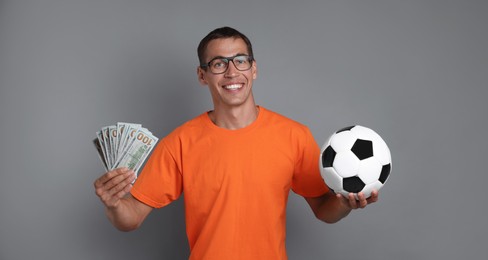 Happy man with money and soccer ball on grey background