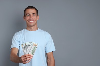 Happy man with money on grey background, space for text