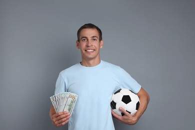 Man with money and soccer ball on grey background