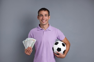 Man with money and soccer ball on grey background