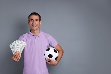 Man with money and soccer ball on grey background, space for text