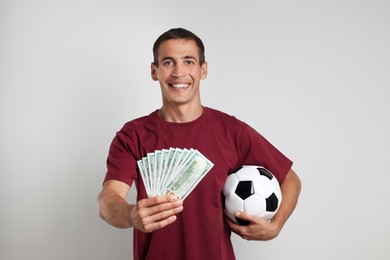 Happy man with money and soccer ball on white background